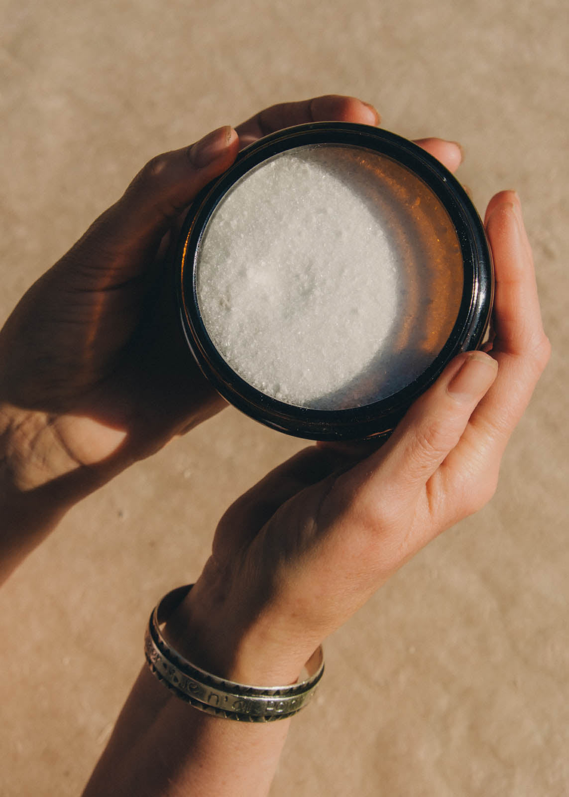 Hands cradling an amber jar of bath salts in the sun
